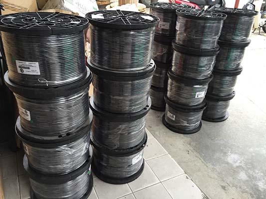 Black spools of wire stacked on a floor, likely in a warehouse or storage area.