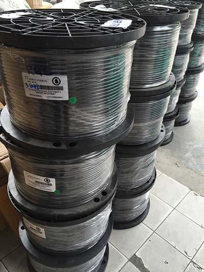 Spools of black cable stacked, wrapped in plastic, labels visible.
