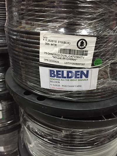Spool of black Belden coaxial cable, wrapped in plastic, with labels, and stacked on other spools.