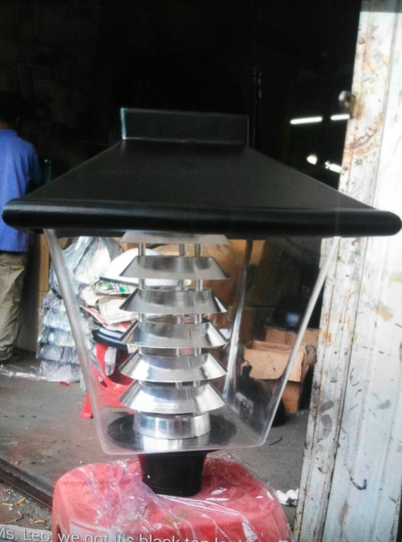 Black and silver outdoor lamp with a clear, geometric enclosure, atop a red stool.