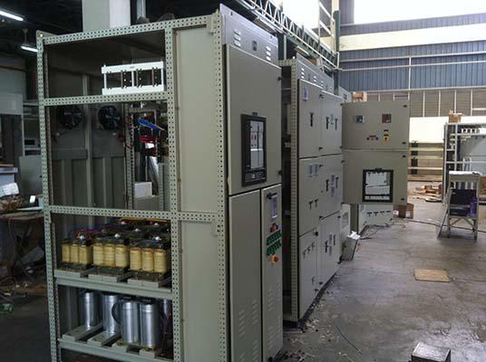 Electrical control panels in a factory setting. Beige cabinets with various components and wiring.
