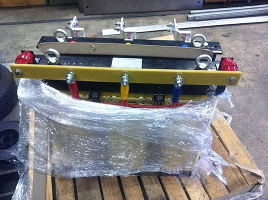 Electrical transformer wrapped in plastic on a wooden pallet, featuring red, yellow, and blue wires.