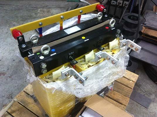 Black electrical equipment, yellow bars, red and blue dots, on a wrapped pallet.