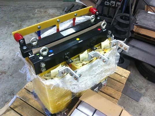 Two large black metal objects with colorful handles, wrapped in plastic on a pallet.