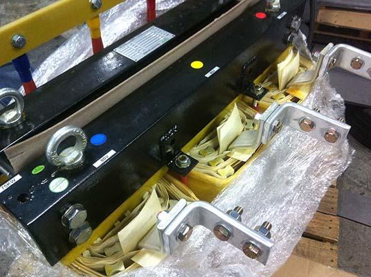 Black and silver industrial equipment with colored dots, bolts, and attached brackets, possibly for overhead lifting.