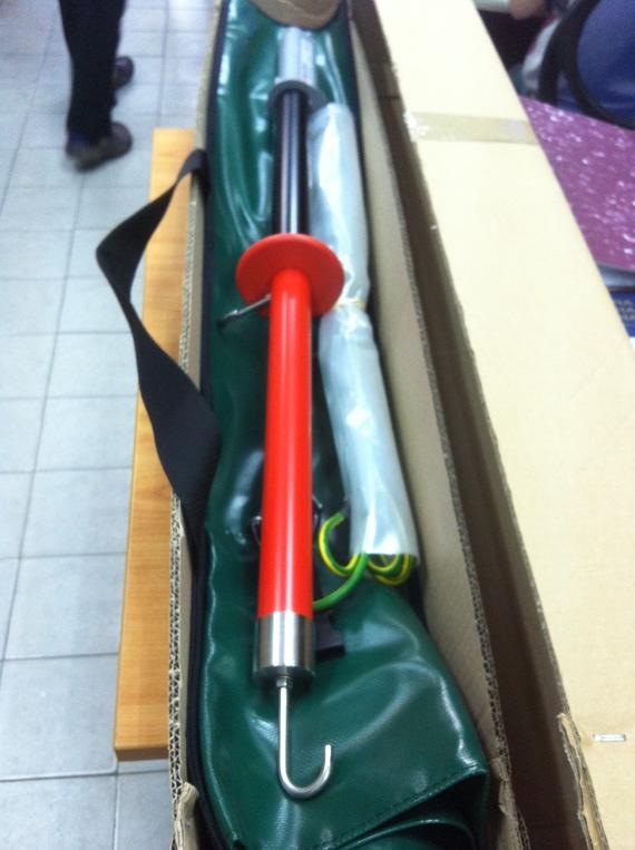 Red and black electrical safety tool inside a green carrying case, in a cardboard box.