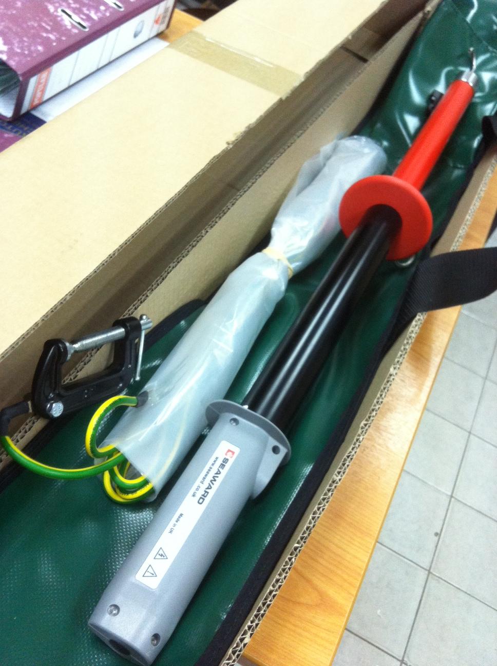 Insulated electrical safety pole, with grounding clamp, stored in a box. Black, red, and green colors.