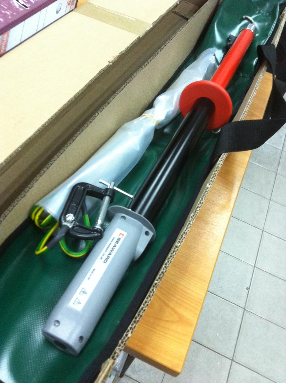 High-voltage safety stick with a clamp and ground wire inside its case.