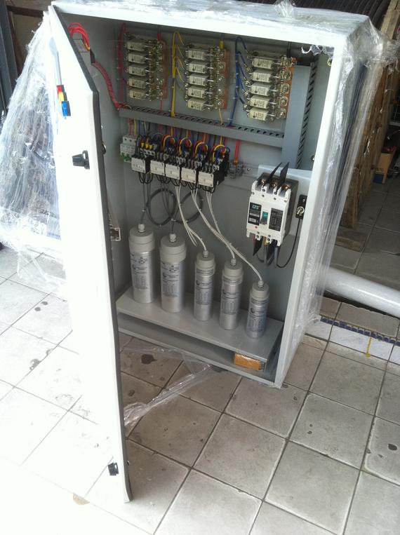 Open electrical cabinet with capacitors and wiring inside.