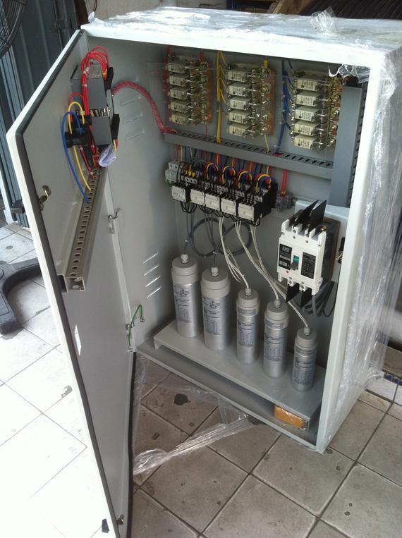 Electrical control panel with open door, showing capacitors, circuit breakers, and wiring.