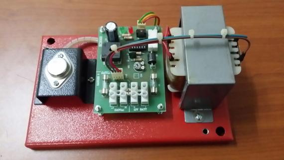 A red base with electronic components: transformer, circuit board, and a black metal enclosure.