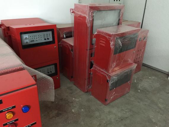 Red electrical control panels, stacked and wrapped, in a warehouse or storage area.