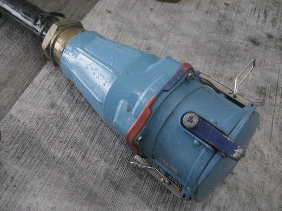 Blue industrial electrical connector, angled, with a metal ring and clasps, on a gray surface.