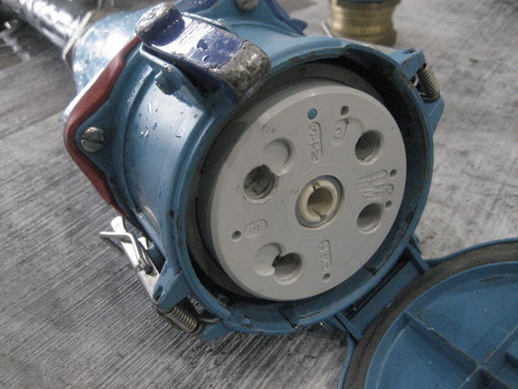 Blue industrial electrical socket with open lid, showing multiple pin holes.