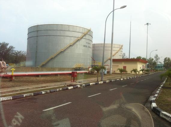 Fuel storage tanks at an industrial site with a road and buildings, on a cloudy day.