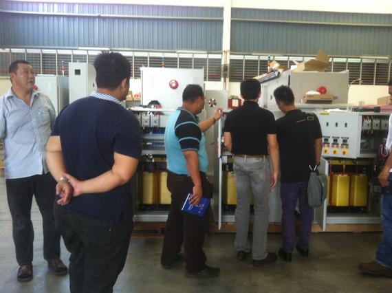 Group of men inspecting electrical equipment in a factory.