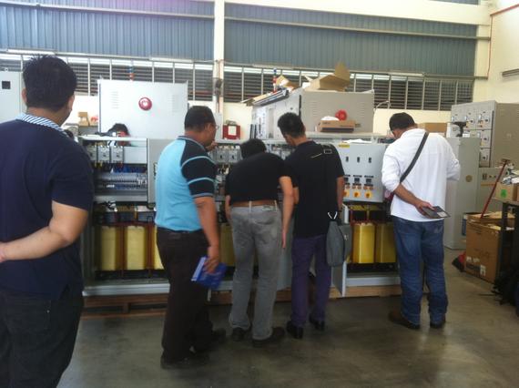 A group of men inspecting a large electrical panel in a warehouse.