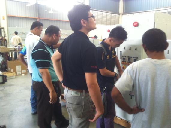 Group of men inspecting machinery in a factory, some looking at the control panel.