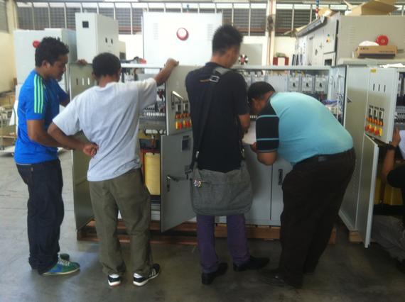 Four men examining electrical equipment in a factory setting.