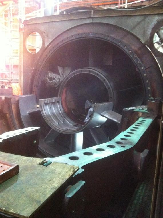 Large industrial turbine, metal, with blades inside, in a factory setting.