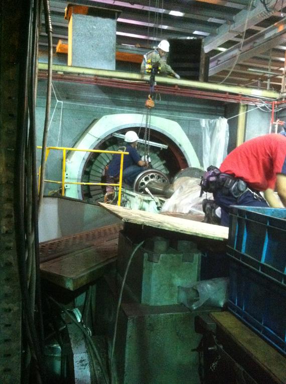 Workers in hard hats near a large industrial machine. Some are on scaffolding, others by the machine.