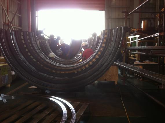 A large, curved metal structure inside a workshop, with workers visible within.