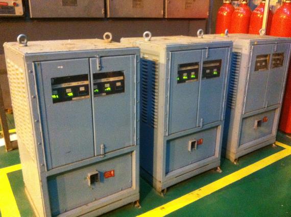 Three blue electrical cabinets in a room with red cylinders, set on yellow lines.