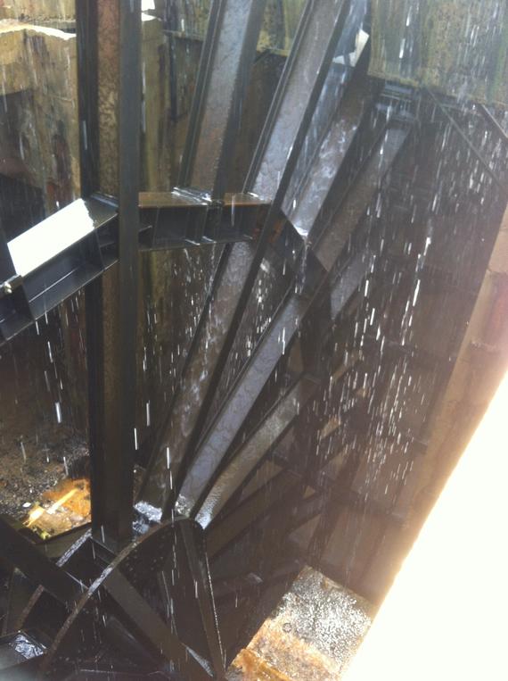 Waterwheel with water cascading over black metal blades, outdoors.