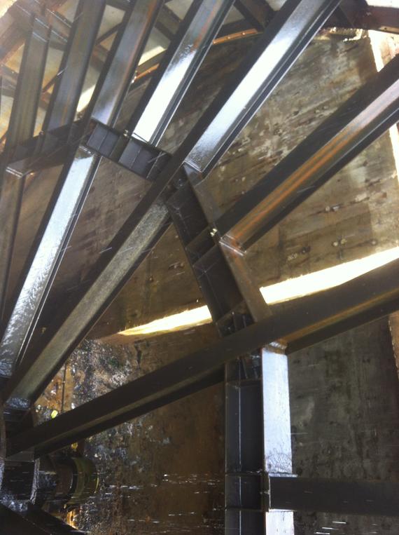 Black metal framework of a water wheel, wet and reflecting light.