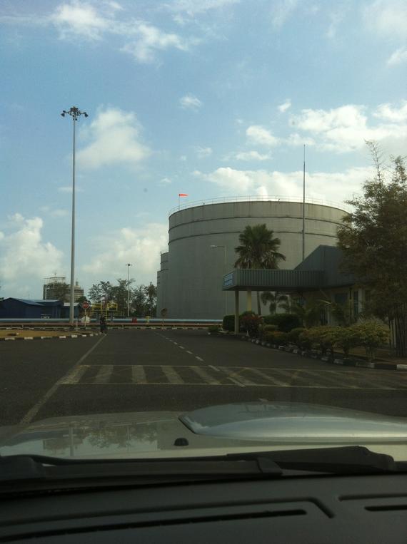 Large cylindrical building with tiered sides, palm trees, and a sky with clouds.