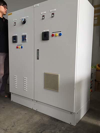 Electric control panel with various gauges, switches, and buttons, in an industrial setting.