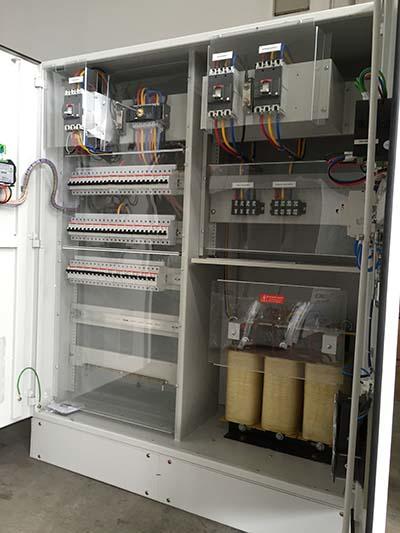 Open electrical cabinet with wiring, circuit breakers, and transformers.
