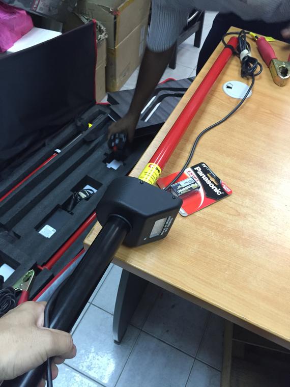 Man holding a black metal pole with a red handle near a table, with a tool case in the background.