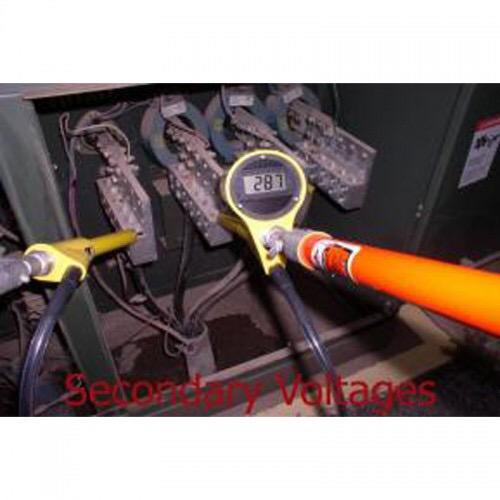 A technician measures secondary voltages with a digital meter on an electrical panel. Yellow and orange cables are visible.