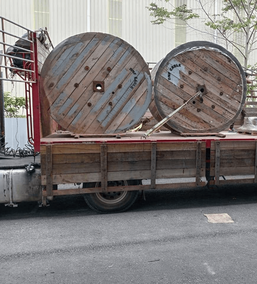 Two large wooden cable spools on a truck bed, parked on a road.