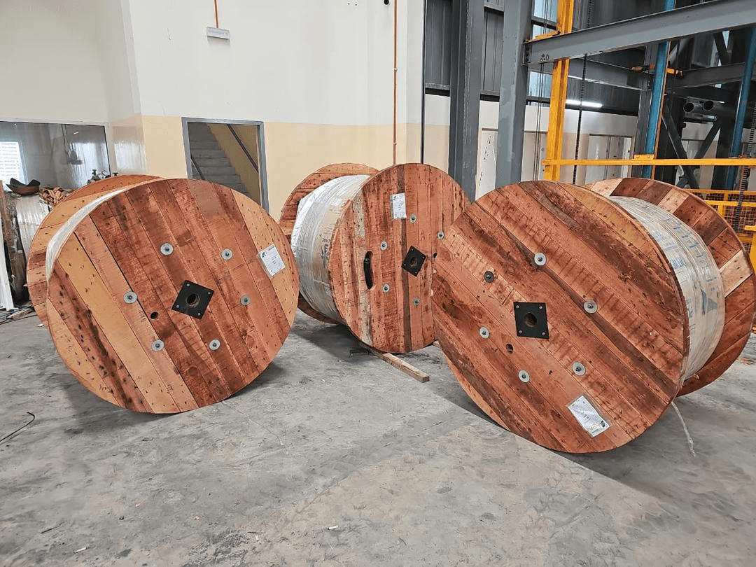 Wooden cable spools lined up on a gray floor inside a factory.