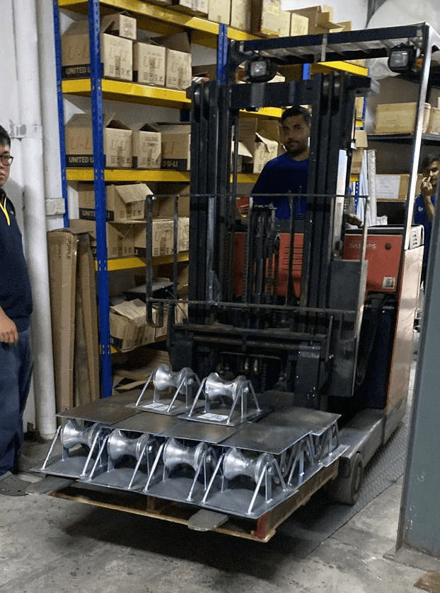Man operating a forklift carrying a pallet of metal objects in a warehouse. Another man stands nearby.