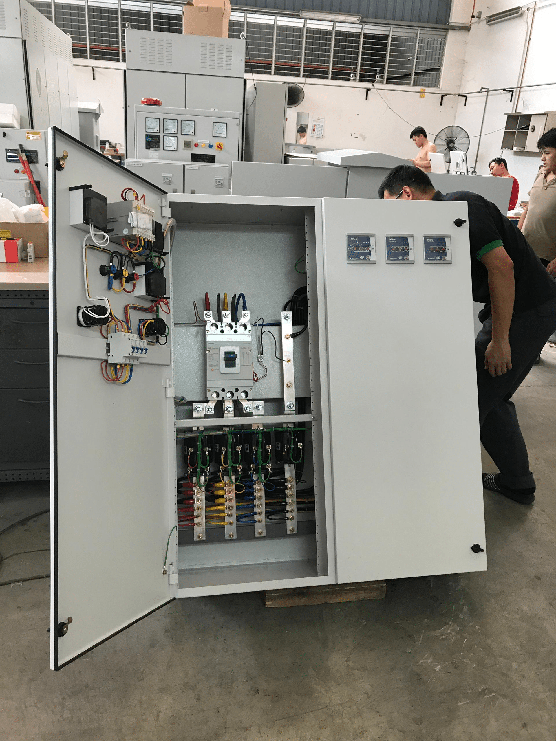 Two men inspecting an open, gray electrical control cabinet in a workshop.