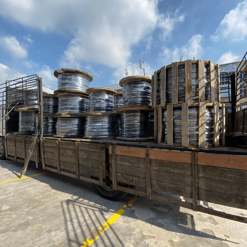 Truck loaded with spools of cable, under a blue sky with clouds.