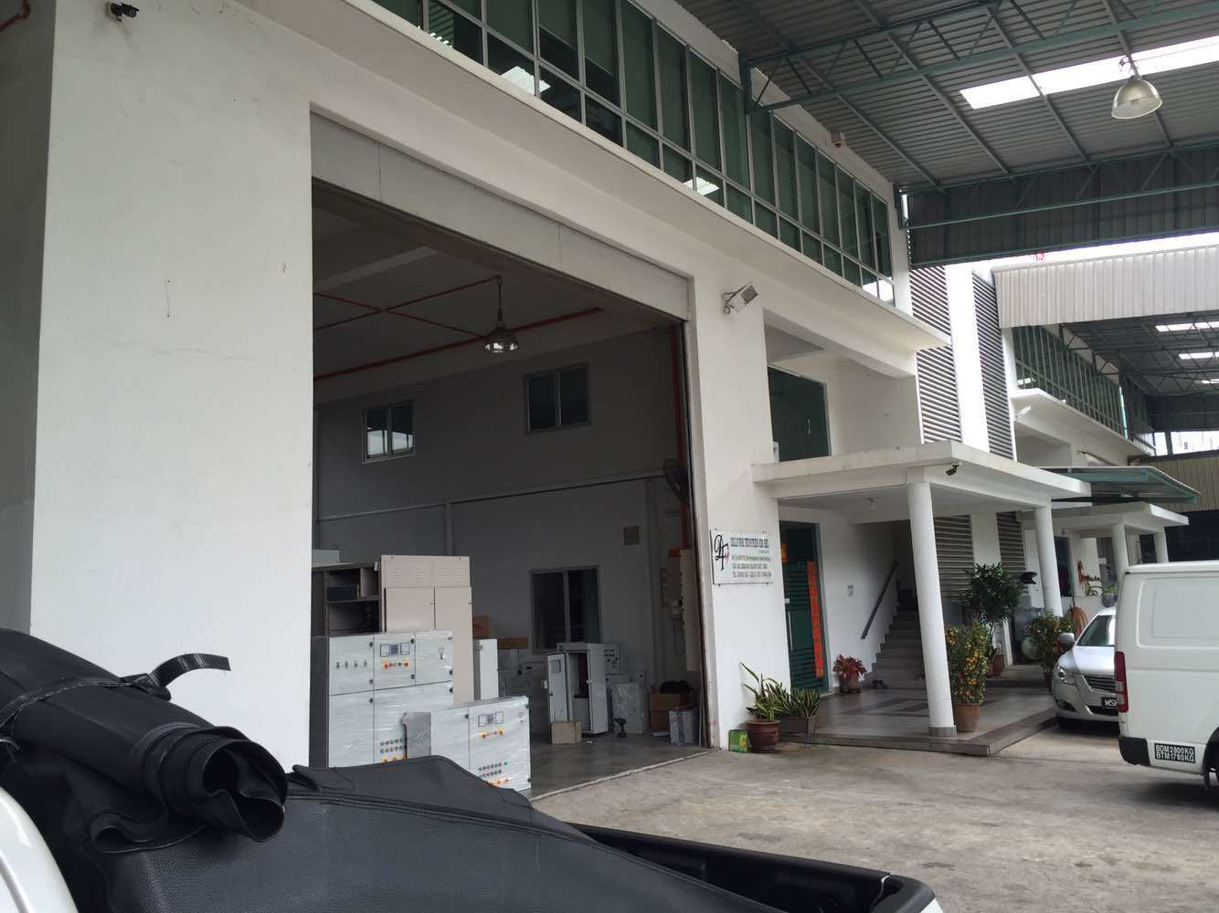 Exterior of a white warehouse with loading bay open, a small entrance, and parked vehicles.