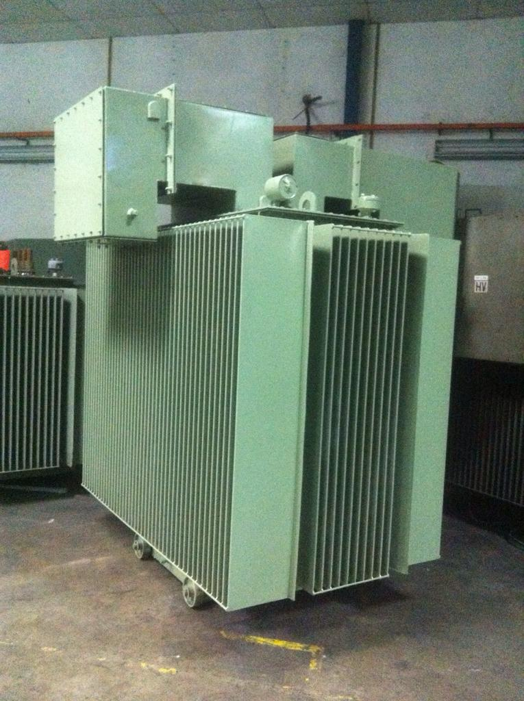 Large green electrical transformer in an industrial setting.