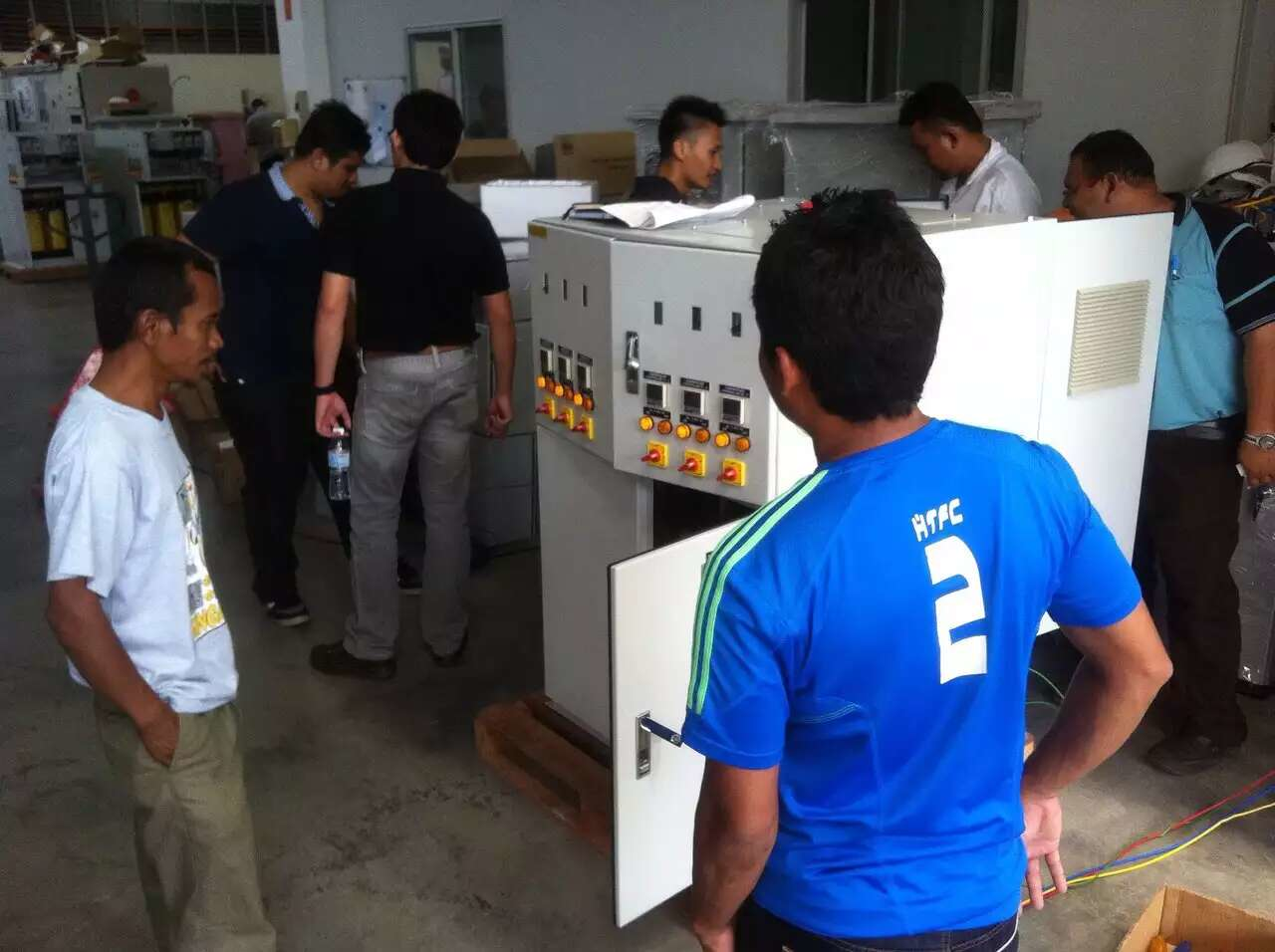 Group of men examining a white industrial machine with control panels in a factory setting.