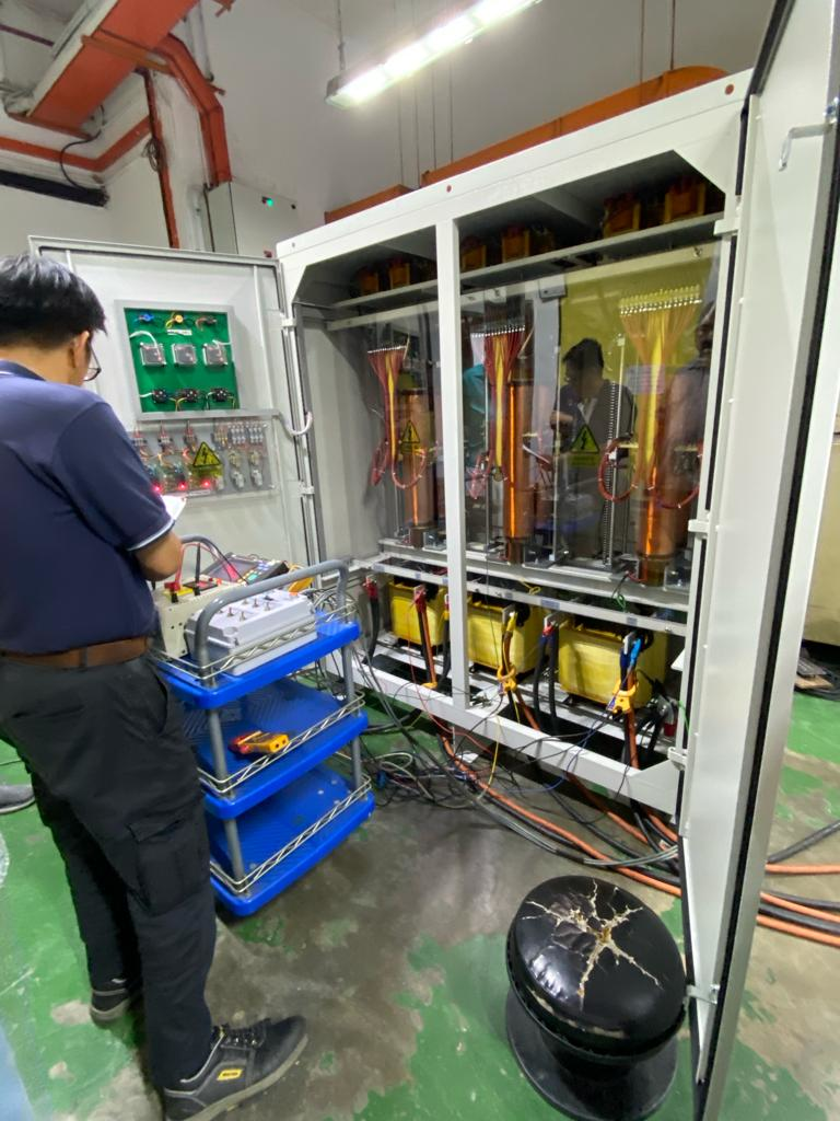 Man working on electrical equipment inside a cabinet. Tools and equipment sit on a blue cart. Setting: indoor.
