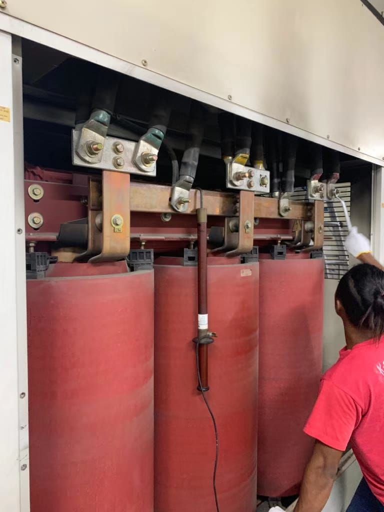 Worker by a red transformer, inside a gray electrical cabinet.