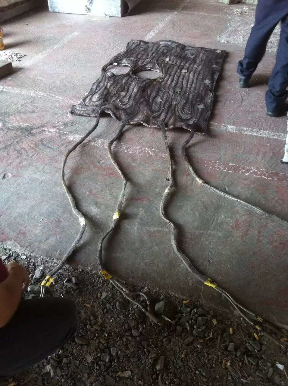 Black mat-like object with four connected cords on a concrete floor. Feet visible in the background.