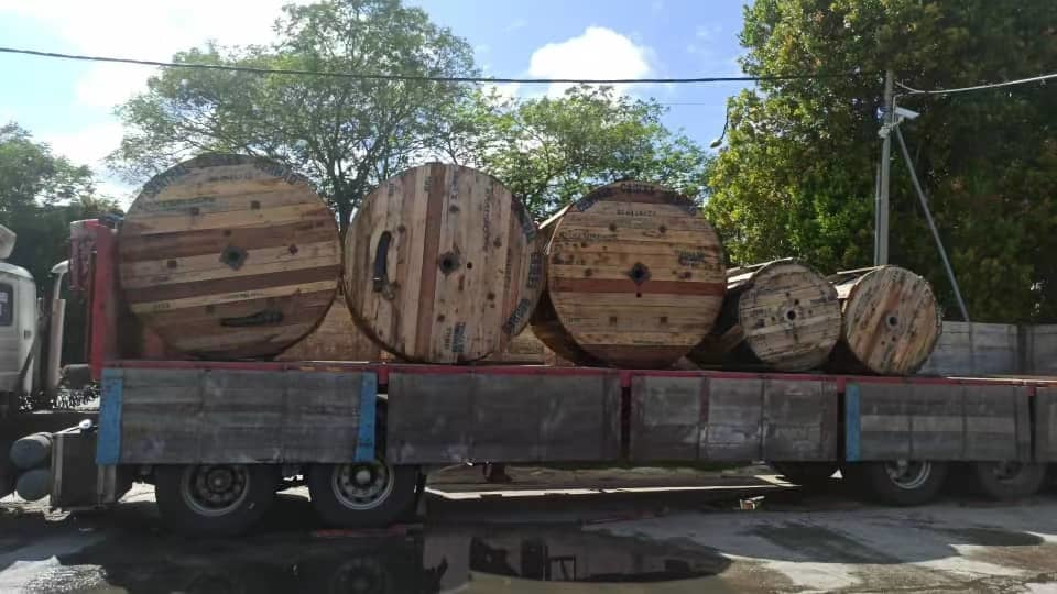 Wooden cable spools loaded on a flatbed truck, outdoors under a blue sky.