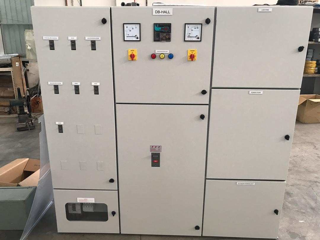 Electrical control panel with gauges, switches, and doors in a factory setting.