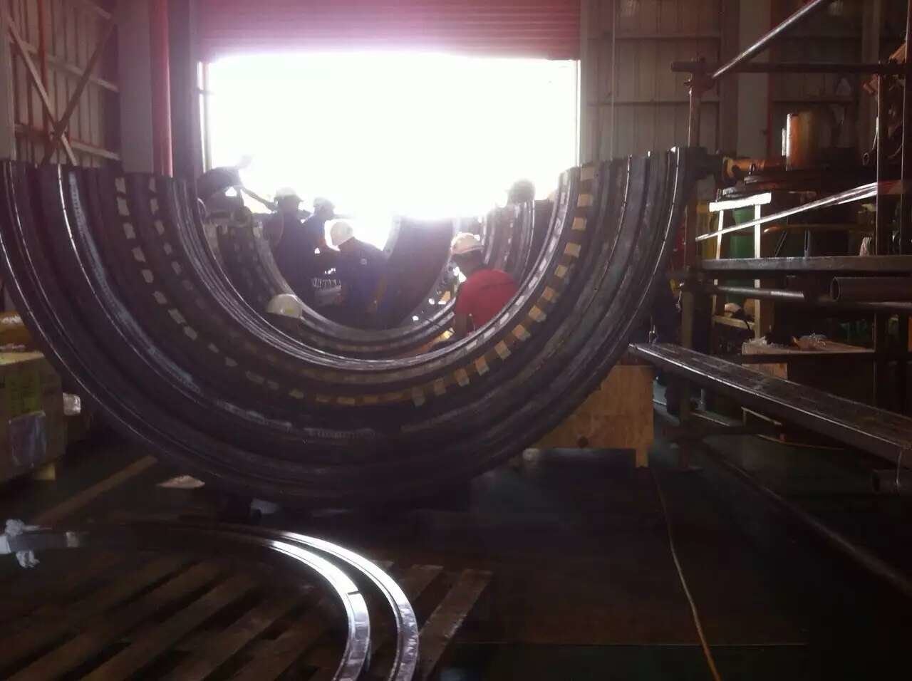Large semi-circular metal rings, possibly machinery components, in a workshop. Bright light shines in background.