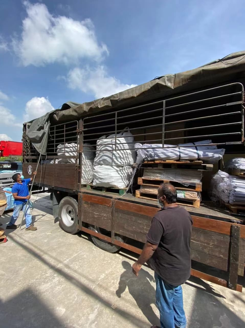 Truck loaded with packaged goods, two men stand near the truck outdoors under a partly cloudy sky.