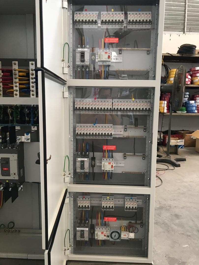 Electrical control panel with circuit breakers, wires, and components, enclosed in a white cabinet.